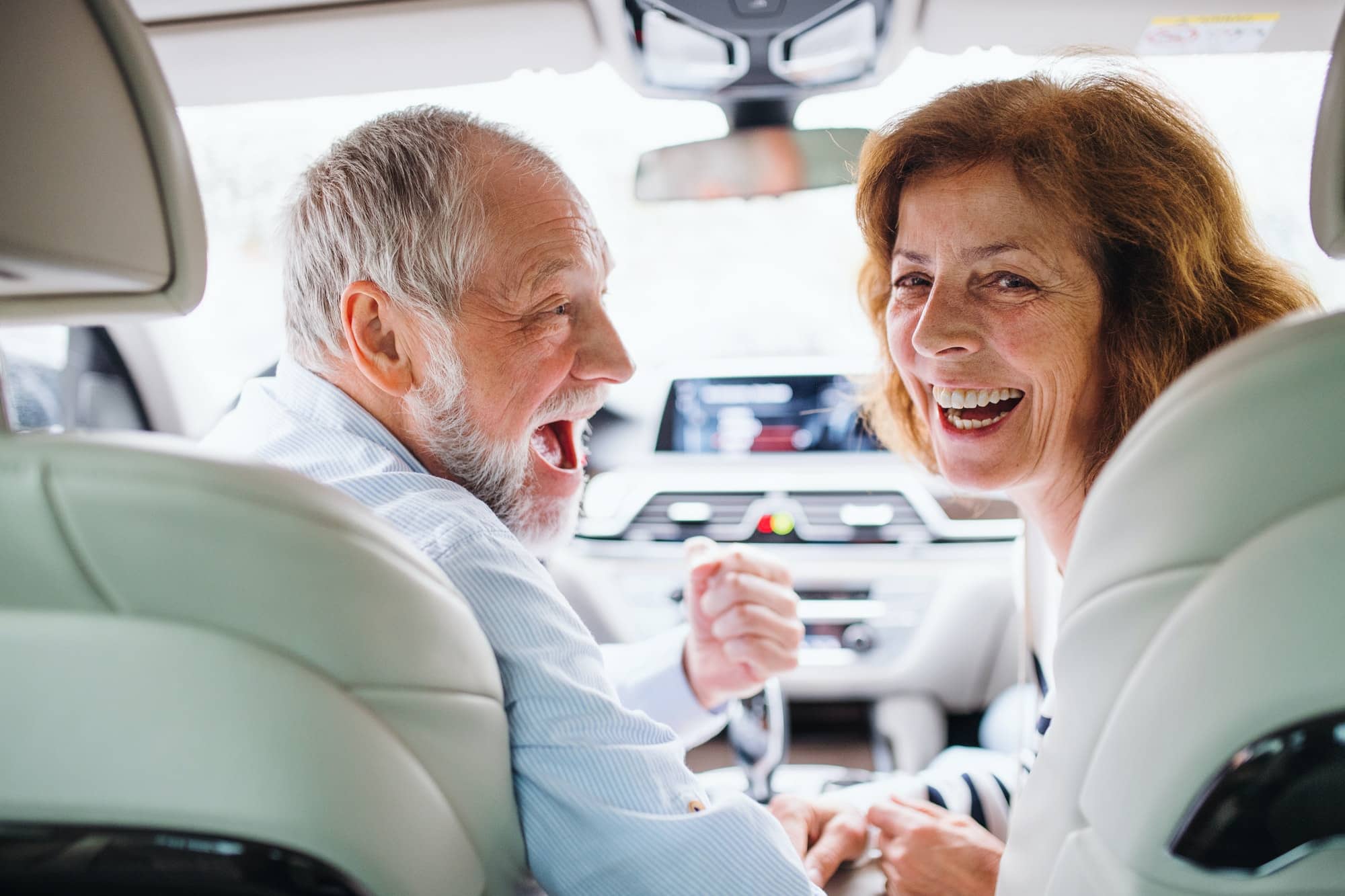 Rear view of happy senior couple sitting in car, looking back